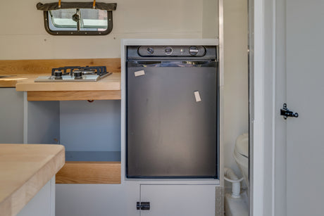 RV rental: Compact kitchen featuring a gas stove, wooden counter, built-in fridge, and small window.