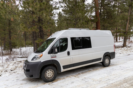 White campervan RV rental on a snowy forest road, set for winter adventures.