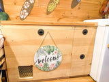 Cozy RV rental interior: A tropical welcome sign on wooden cabinetry with secure latches and ventilation.
