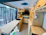 Modern rv rental camper van with light wood interior, kitchen, bed, and a scenic outdoor view.