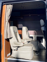 Spacious RV rental interior featuring two comfortable captain's chairs, wood cabinetry, and a patterned curtain.