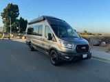 This stylish gray Ford Transit camper van, ideal for RV rental adventures, is parked on a sunny day with scenic views.
