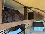 RV rental interior: plush blanket in overhead storage with gas struts, next to a blackout window shade and wall basket. Camper comfort.