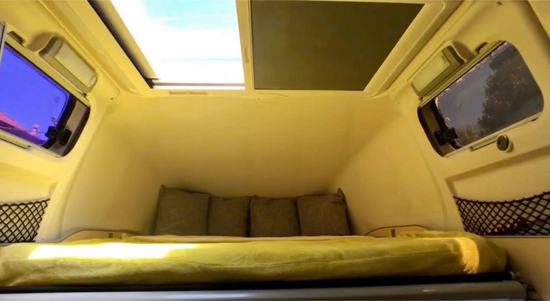 Cozy RV rental interior with a bed, pillows, large skylight, windows, and storage nets. Perfect for your next adventure. — photo 16