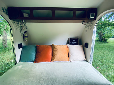 Homey RV rental bedroom: cozy bed with vibrant pillows, overhead storage, and a relaxing view of nature.