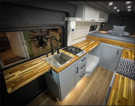 Modern RV rental: a stylish van conversion with a full kitchen, wood counters, comfortable bed, and smart storage.