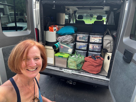 Smiling woman shows off her organized, packed RV rental camper van, ready for an adventure.