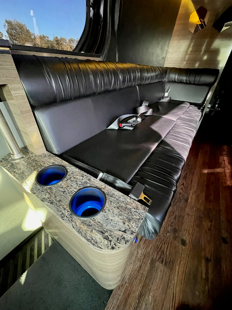 Spacious RV rental interior featuring black leather bench seating, illuminated cup holders, and a scenic window view. — photo 20