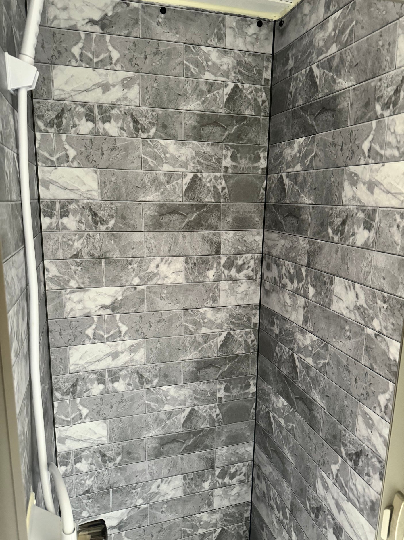 Modern grey & white marble-look tiled shower interior in an RV rental, featuring a white shower rail.