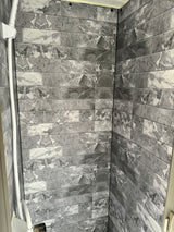 Modern grey & white marble-look tiled shower interior in an RV rental, featuring a white shower rail.