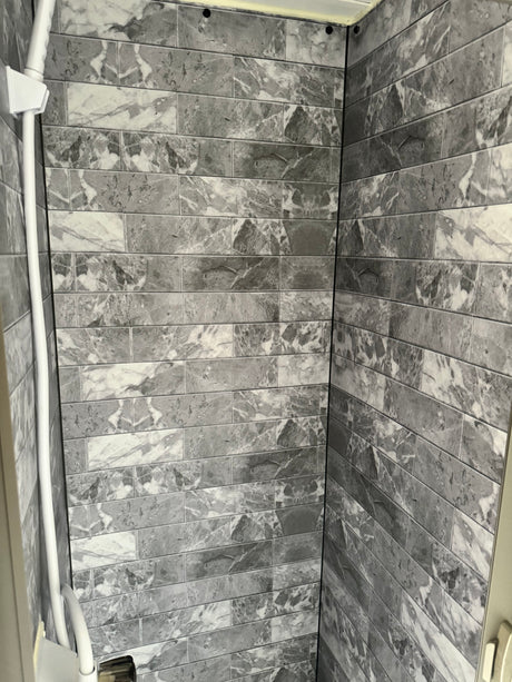 Modern grey & white marble-look tiled shower interior in an RV rental, featuring a white shower rail.