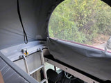 RV rental interior: Pop-top bunk with ladder & scenic view through the window, inside a camper van.