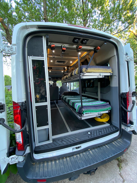View into an RV rental van, showcasing its modular interior with upper and lower bunk beds and aluminum frame.
