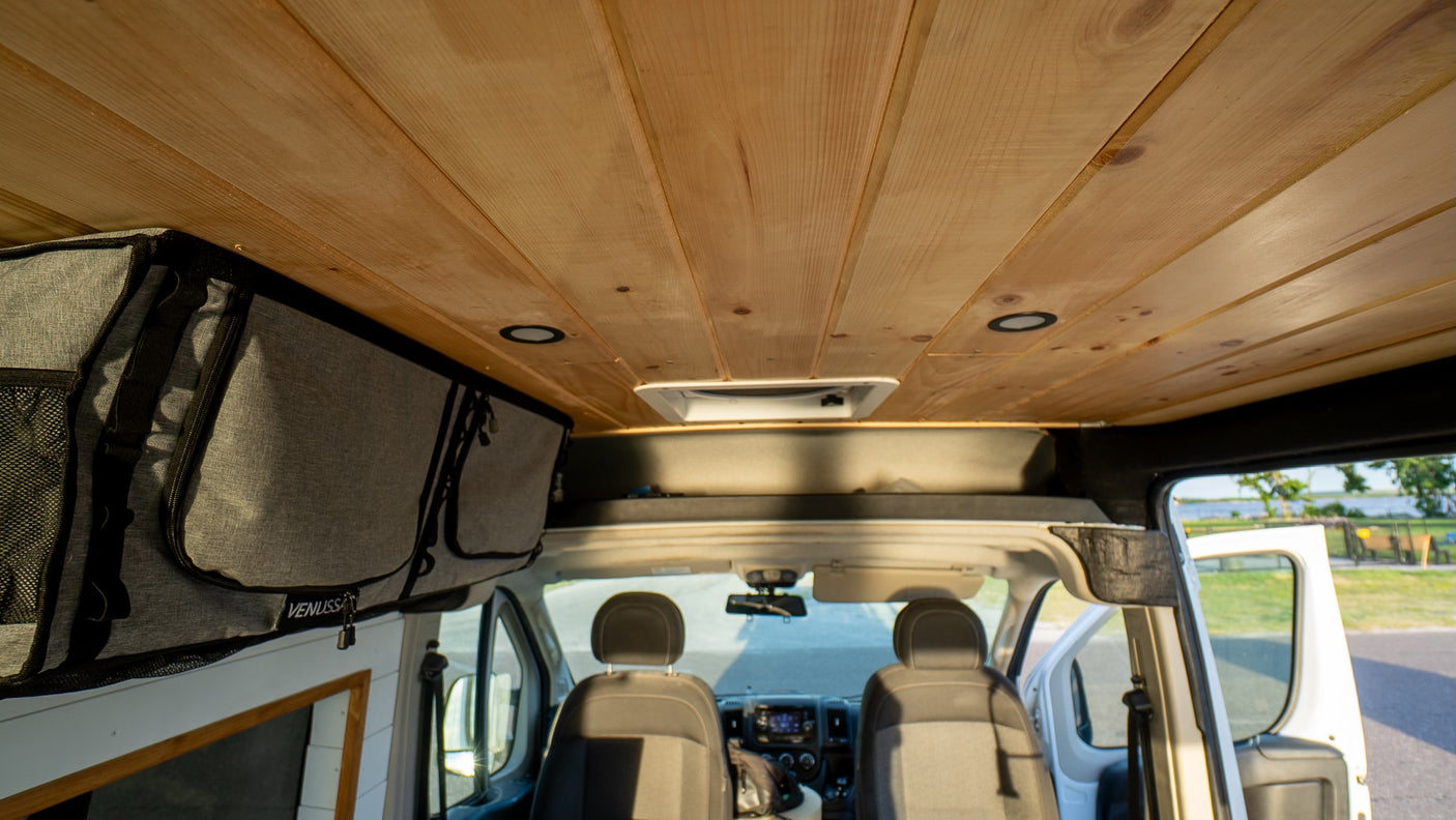 Inside a custom RV rental van: warm wooden ceiling, smart overhead storage, & front cabin. Ready for adventure!