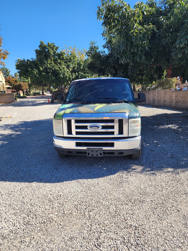 Front view of a green Ford van, excellent for RV rental, parked on gravel under a sunny blue sky. — photo 4