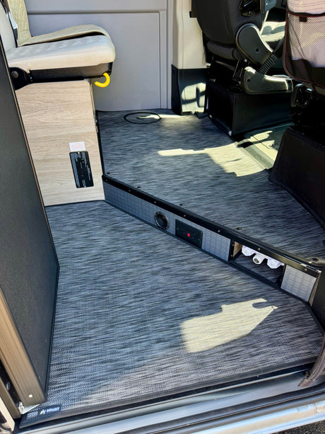 Inside an rv rental with durable patterned flooring, custom seating, and a utility panel with plumbing access.