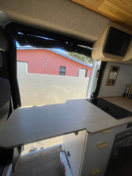 Modern RV rental interior with sleek kitchen, extending counter, and accessible controls. A fire extinguisher is mounted by the window.