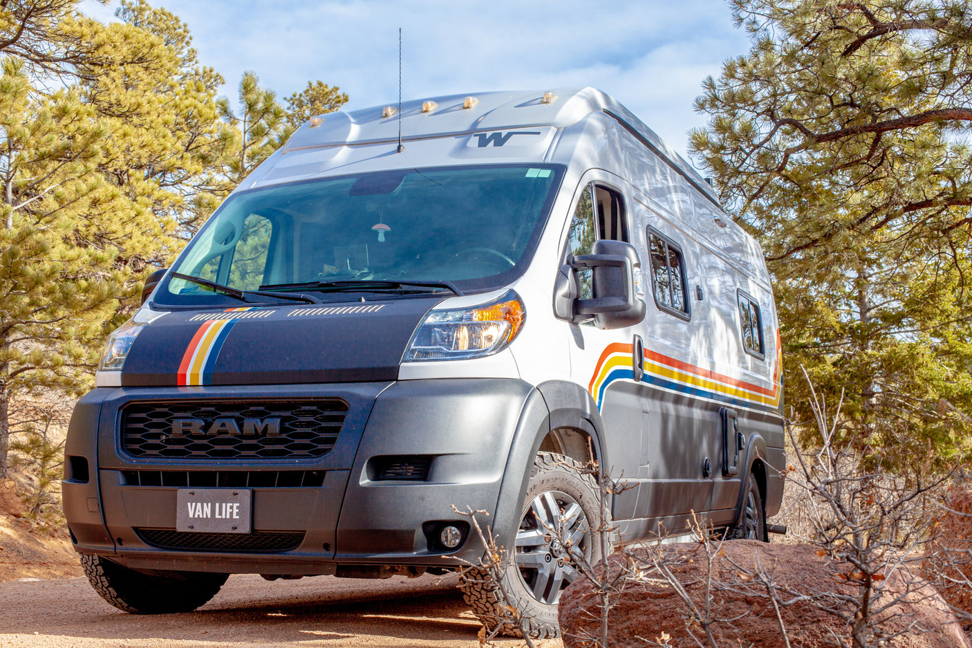 This stylish camper van, available for RV rental, offers the perfect van life adventure parked among pine trees.