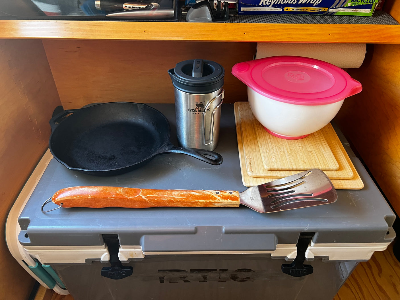 Organized RV rental kitchen, featuring a cast iron pan, Stanley mug, mixing bowl, and utensils. Ready for camping meals.