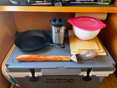 Organized RV rental kitchen, featuring a cast iron pan, Stanley mug, mixing bowl, and utensils. Ready for camping meals.
