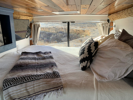 Cozy RV rental interior with a comfortable bed and stunning desert views through the back window. Perfect for adventure.