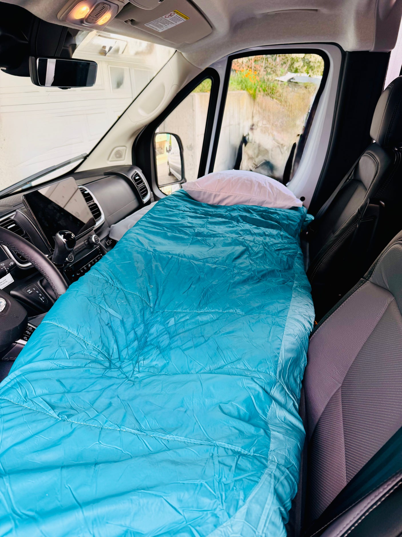RV rental interior: front seats converted to a bed with a blue sleeping bag & white pillow, ready for a road trip.