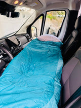 RV rental interior: front seats converted to a bed with a blue sleeping bag & white pillow, ready for a road trip.