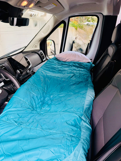 RV rental interior: front seats converted to a bed with a blue sleeping bag & white pillow, ready for a road trip.