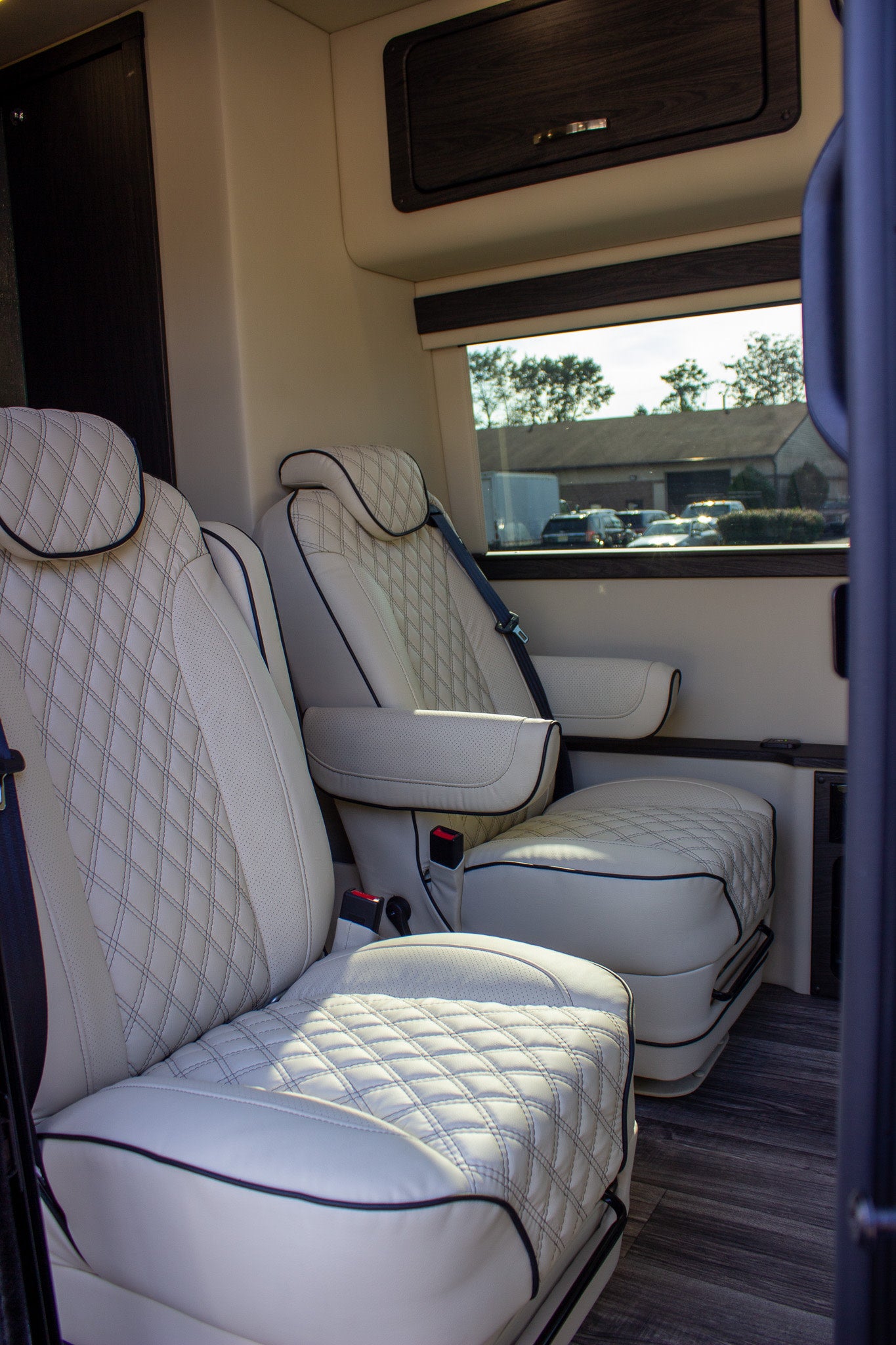 Luxurious RV rental interior: cream diamond-quilted captain's chairs, dark wood cabinetry, and sleek wood-look flooring.
