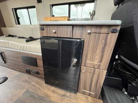 This rv rental features a compact kitchen with a built-in fridge, sink, and comfortable bench seating inside.