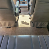 Spacious RV rental interior featuring tan captain's chairs, a central console, and a rear bench seat with carpeted floor.