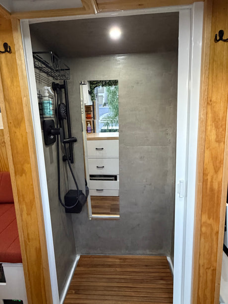 Modern RV rental shower with sleek black fixtures, grey walls, and a wooden slatted floor. Compact and refreshing.