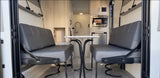 This RV rental interior features a compact living area with facing benches, a table, and a small kitchen.