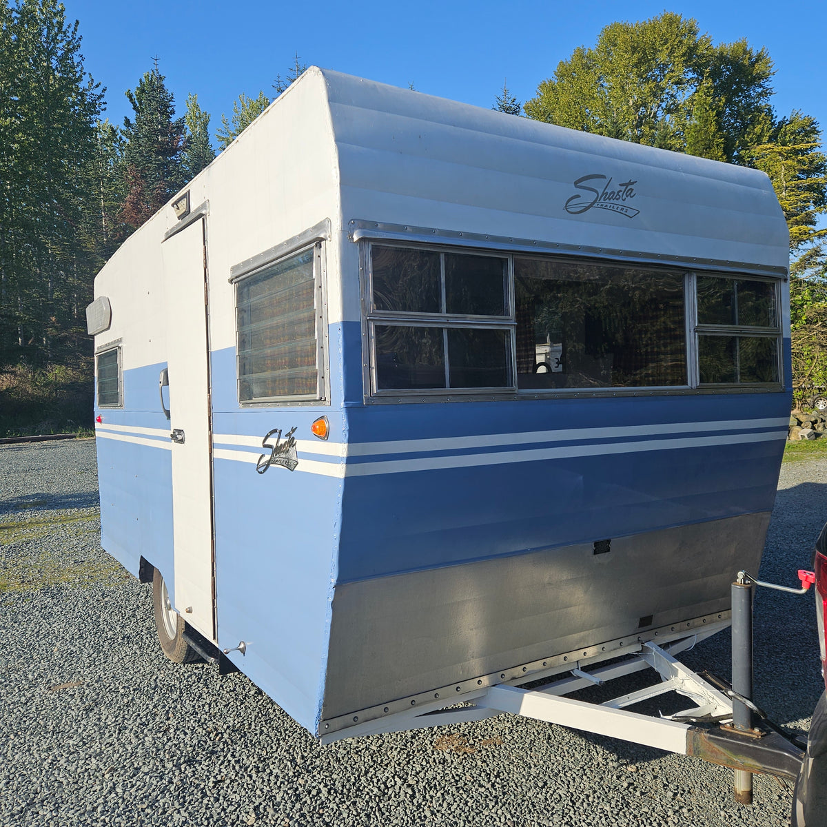 This charming blue and white Shasta travel trailer, perfect for your next RV rental, is parked on gravel. — photo 3