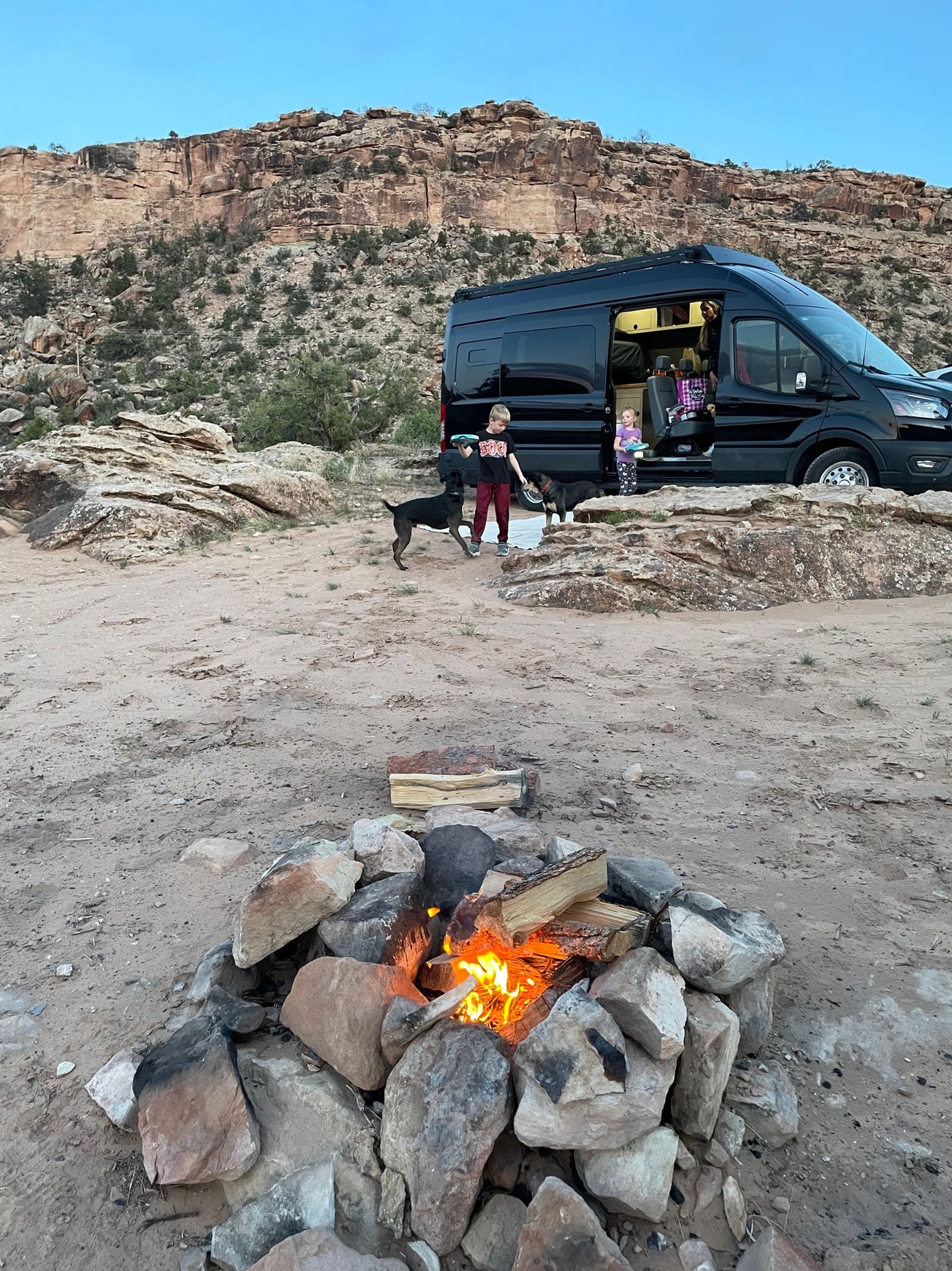  surrounded by forests & vibrant sky. A perfect RV rental trip for family outdoor fun.|An RV rental van and several mountain bikes are parked on a gravel campsite with a dog running in the hilly background.|Experience stunning autumn colors on a mountain dirt road — photo 8