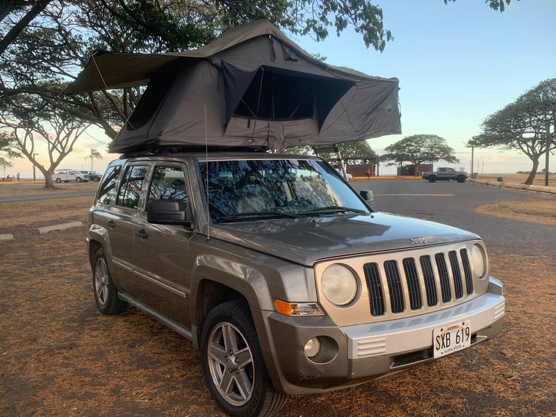 A grey Jeep Patriot with a rooftop tent, available for RV rental in Hawaii, parked for camping near the ocean. — photo 20