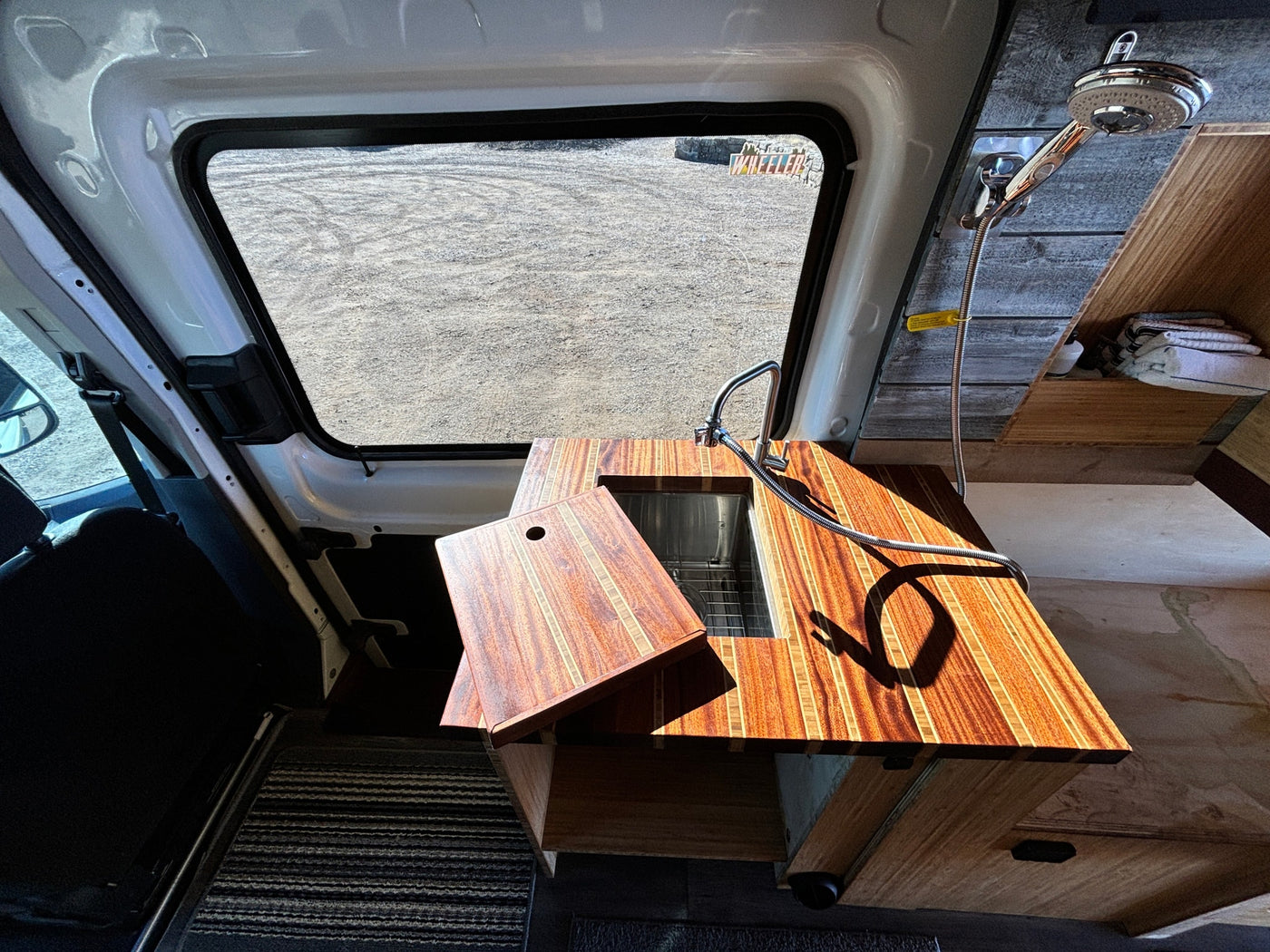 Inside an RV rental camper van: a modern wood countertop with sink, faucet, and a wall-mounted shower head for convenience. — photo 13