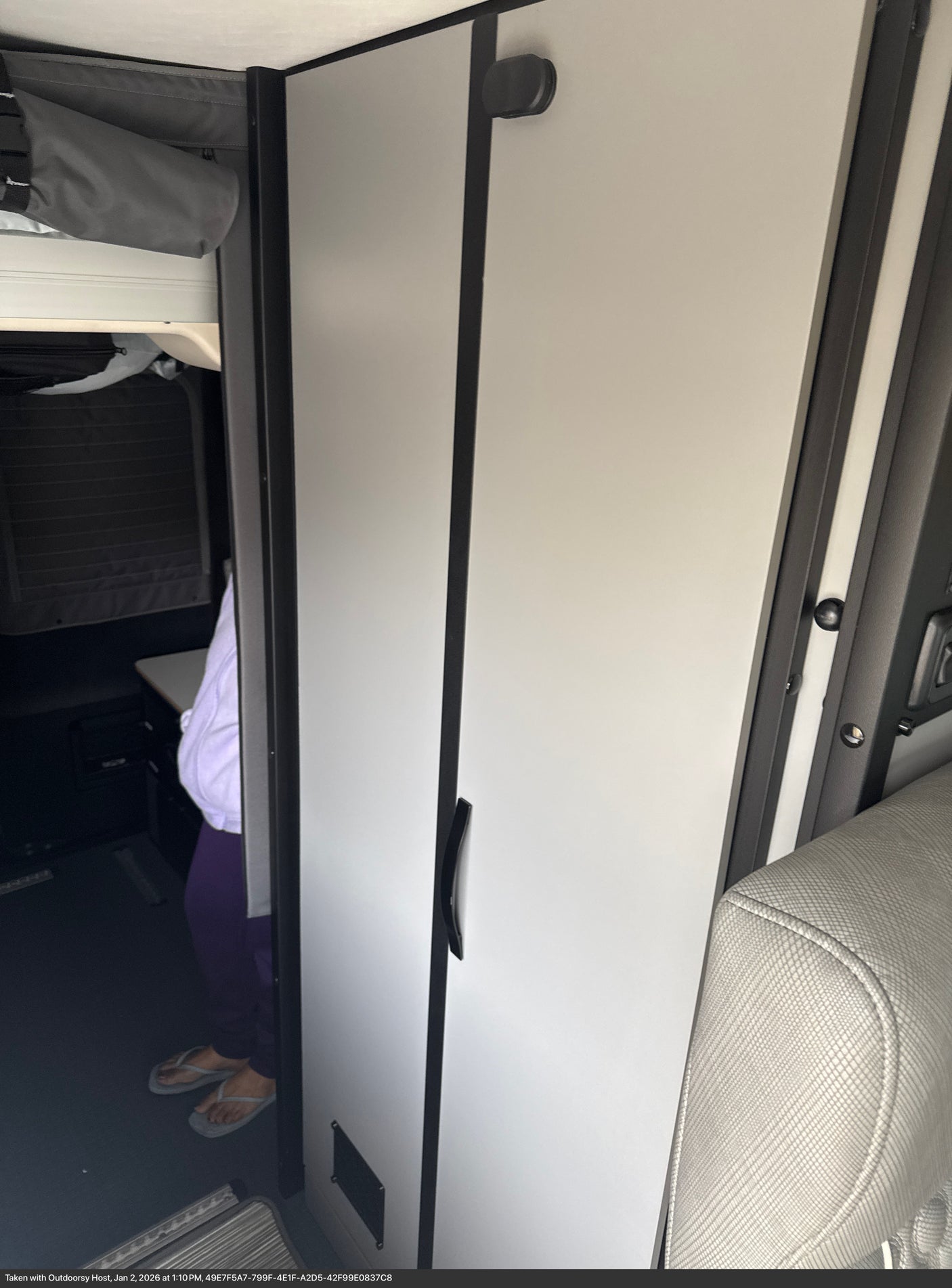 Glimpse into an rv rental interior with white cabinets, overhead storage, and a person's feet on the dark floor.