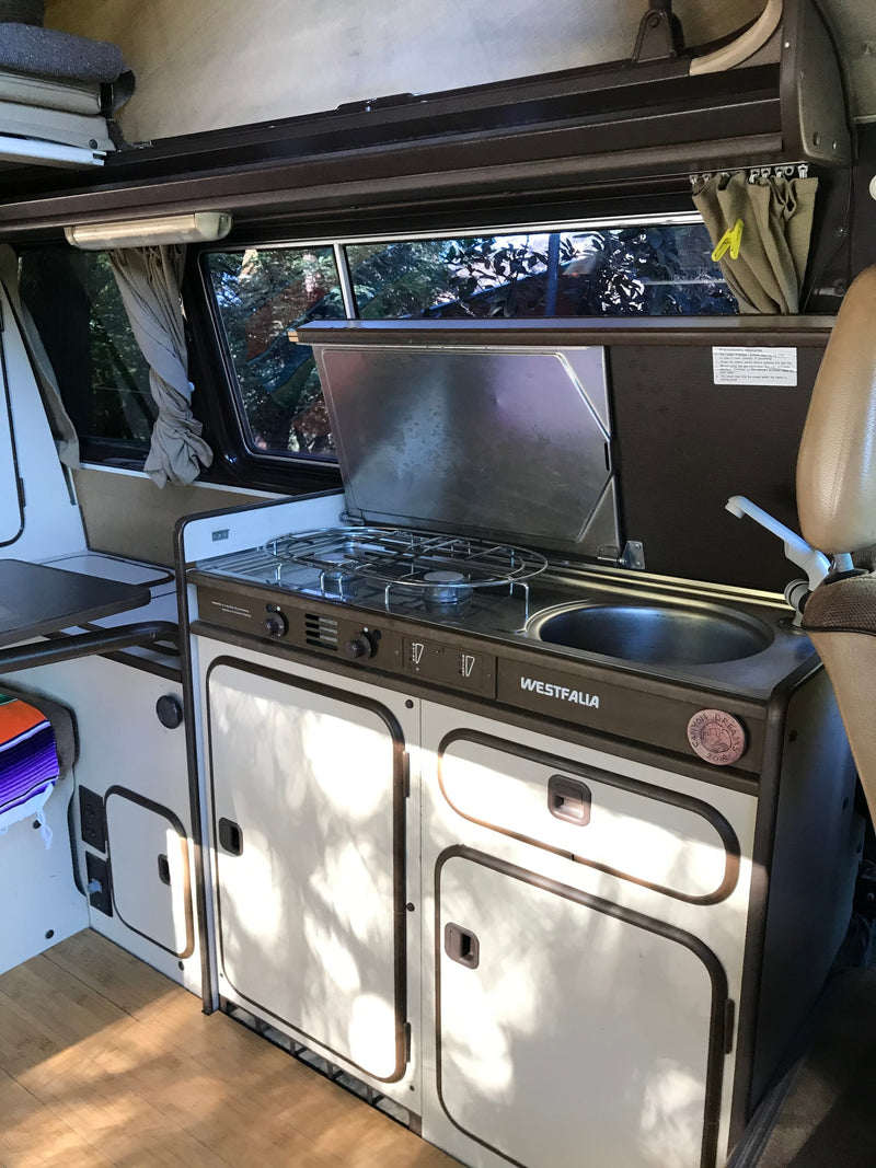  featuring a brown camper van with pop-top roof and a natural sea arch.|Inside an RV rental: A Westfalia camper van kitchen with stove — photo 2