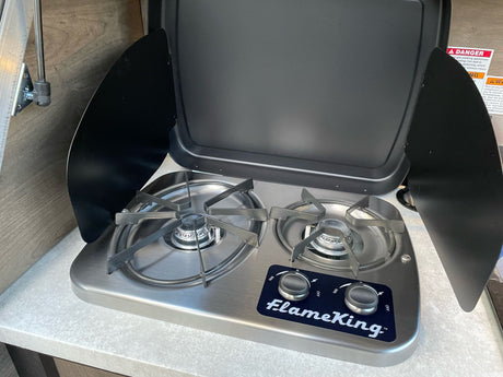A compact, stainless steel Flame King two-burner gas stove with its cover open, found in an RV rental kitchen.