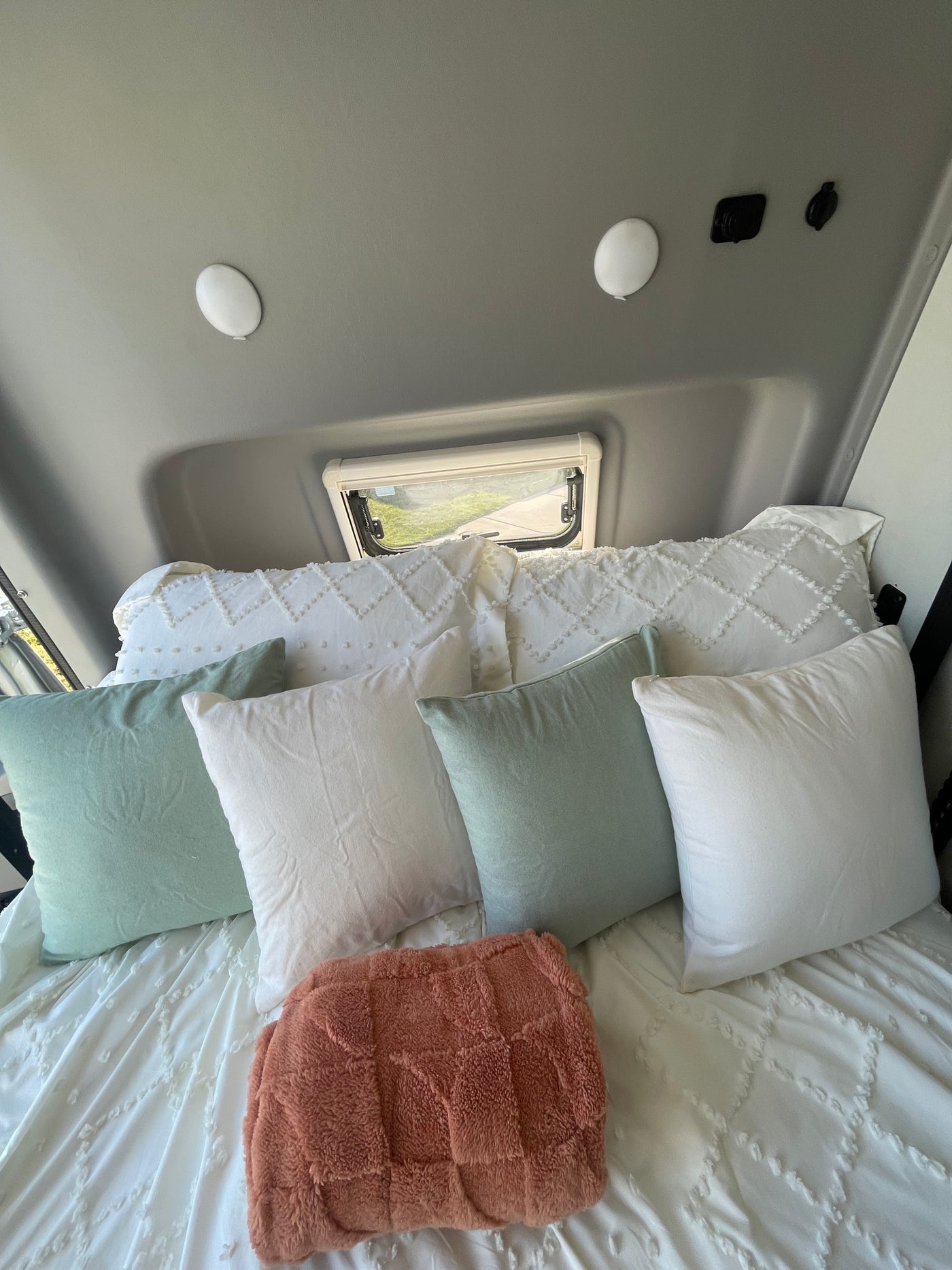 Cozy RV rental bedroom featuring a bed with textured white bedding, soft green and white pillows, and a plush rust blanket. — photo 8