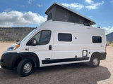 White pop-top camper van, ideal for your next rv rental adventure. Parked outdoors with mountains in view.