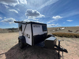 White & black TigerMoth compact RV rental parked on a dirt hill with rocky terrain, under a partly cloudy sky.