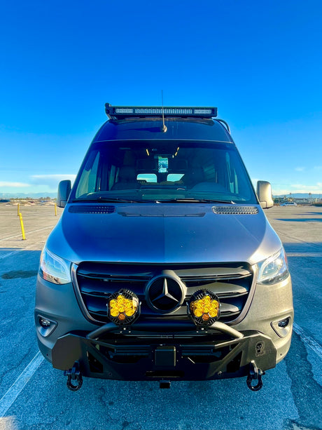 A modified Mercedes Sprinter camper van, equipped with custom lights & bumper, available for rv rental, under a clear sky.