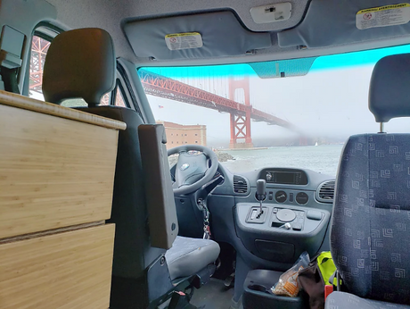Experience a scenic RV rental view of the Golden Gate Bridge through the fog from inside a converted van, featuring a wooden cabinet.