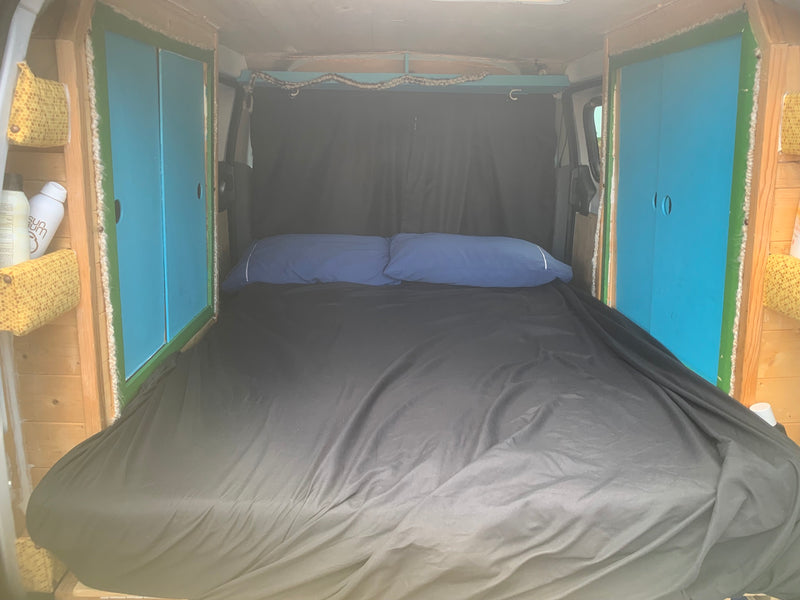  a full bed with black sheets & blue pillows. Wood panels & storage visible on sides.|Adventure awaits! This rv rental shows a camper van with open rear revealing a bed — photo 14