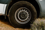 Close-up of an RV rental van's tire and wheel on a dirt path, a Mercedes logo visible on the hubcap.
