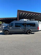 A dark gray Sprinter-style camper van, labeled "Sanctuary", parked under covered storage. Perfect for rv rental trips.