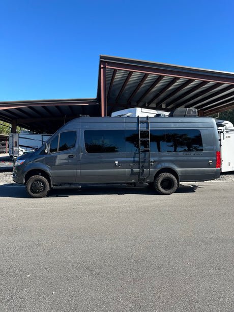 A dark gray Sprinter-style camper van, labeled "Sanctuary", parked under covered storage. Perfect for rv rental trips.