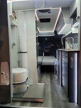 Inside a sleek rv rental: compact wet bath, kitchen with tiled backsplash, bright LED lighting, and convertible seating.